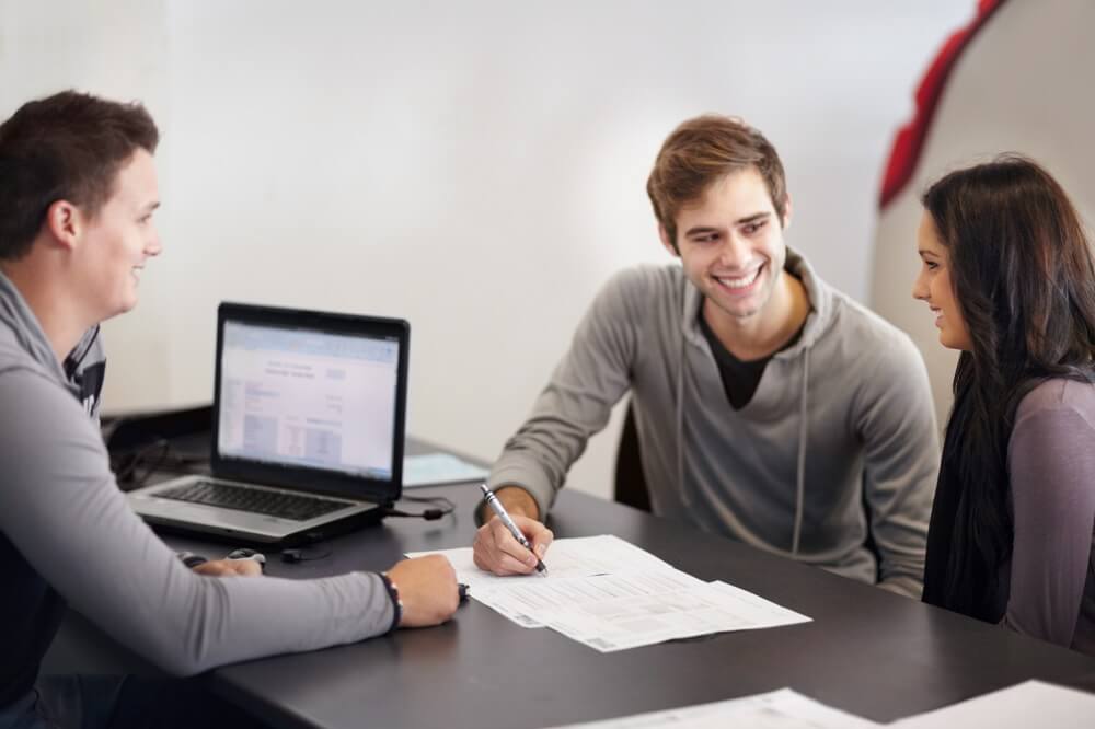 Couple signing paperwork across from man with laptop