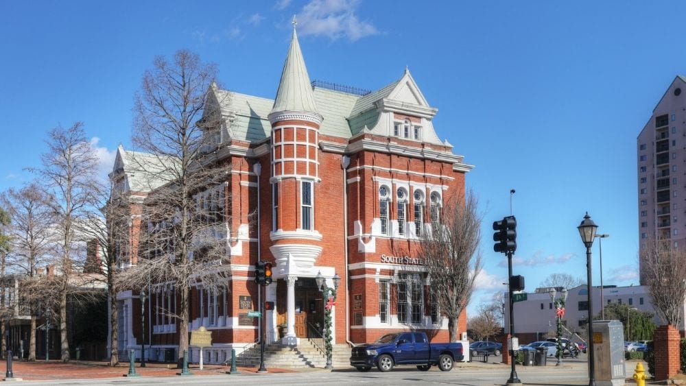 A Romanesque Victorian building made from red brick sits on the corner of a street on a clear day.