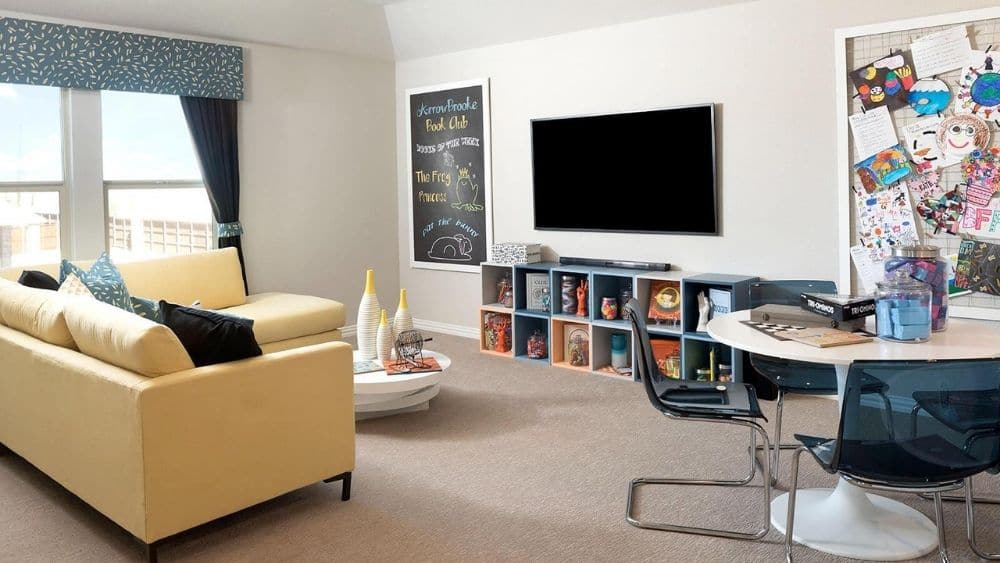 Kid’s playroom with a small yellow couch, a TV, and a bulletin board filled with art.