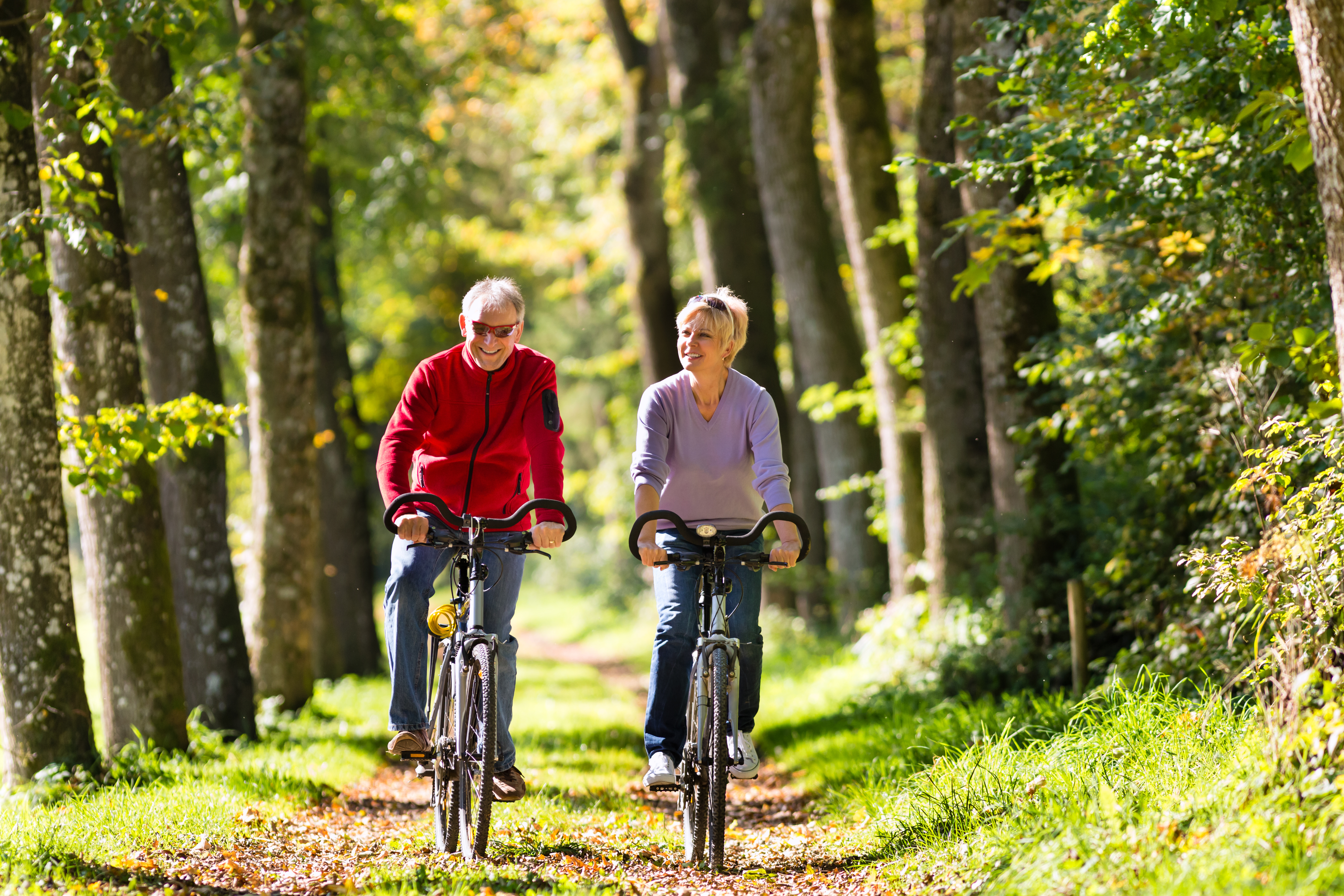 senior couple riding bikes along a wooded trail