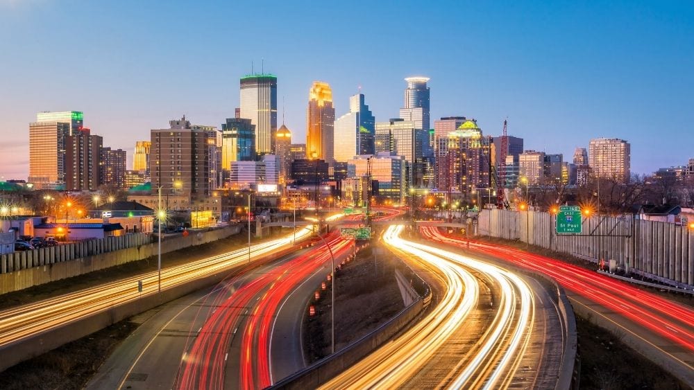 A skyline view of buildings in Minneaopolis, Minnesota, with lines of lights suggesting cars driving quickly