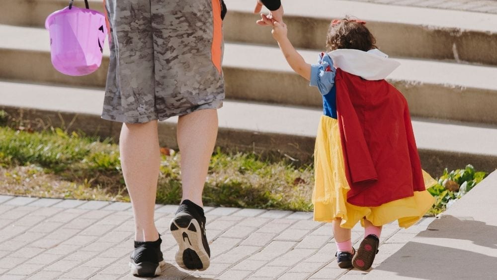 A picture from behind of a toddler dressed up as Snow White, holding the hand of an adult.