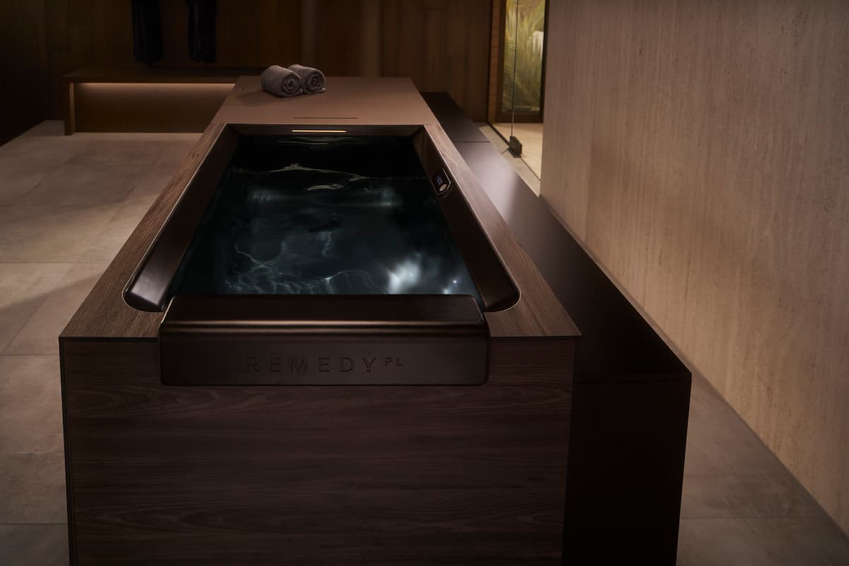 cold plunge tub with black interior and dark brown wood surround, with rolled towels on top