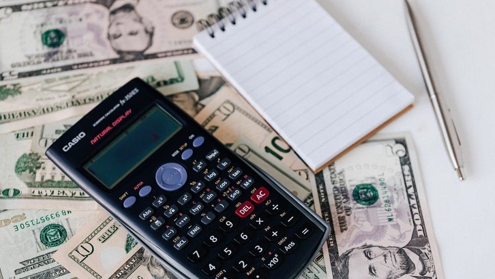 Desk with a notepad and pen, money, and a calculator.