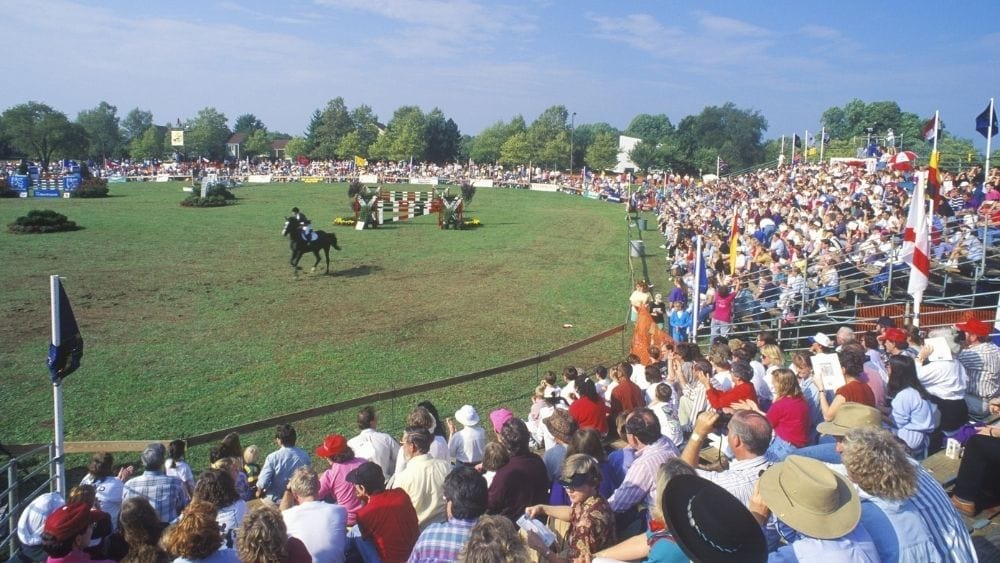 A crowd watching a horse show competition on a sunny day.