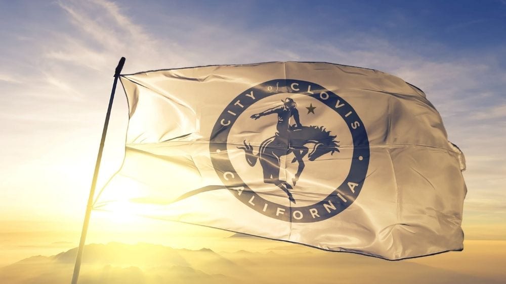 White flag with a seal that says “City of Clovis” around a cowboy on a horse.