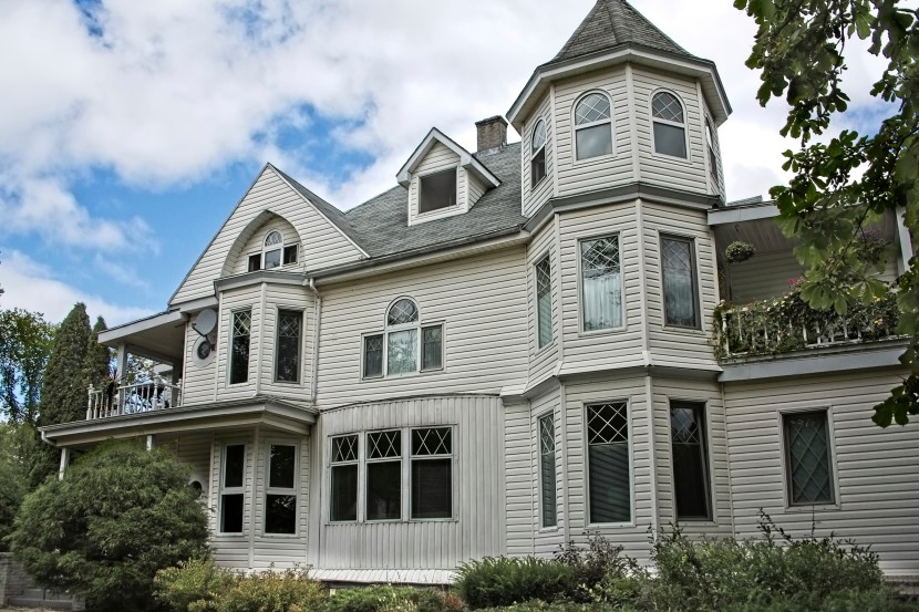 Grey Victorian-style house with siding, dormer windows, bay windows, turrets and a porch