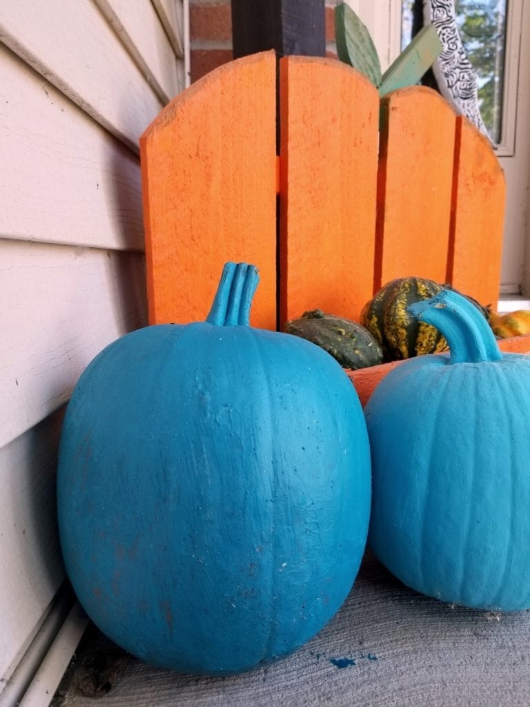 Teal pumpkins in front of an orange wooden pumpkin.