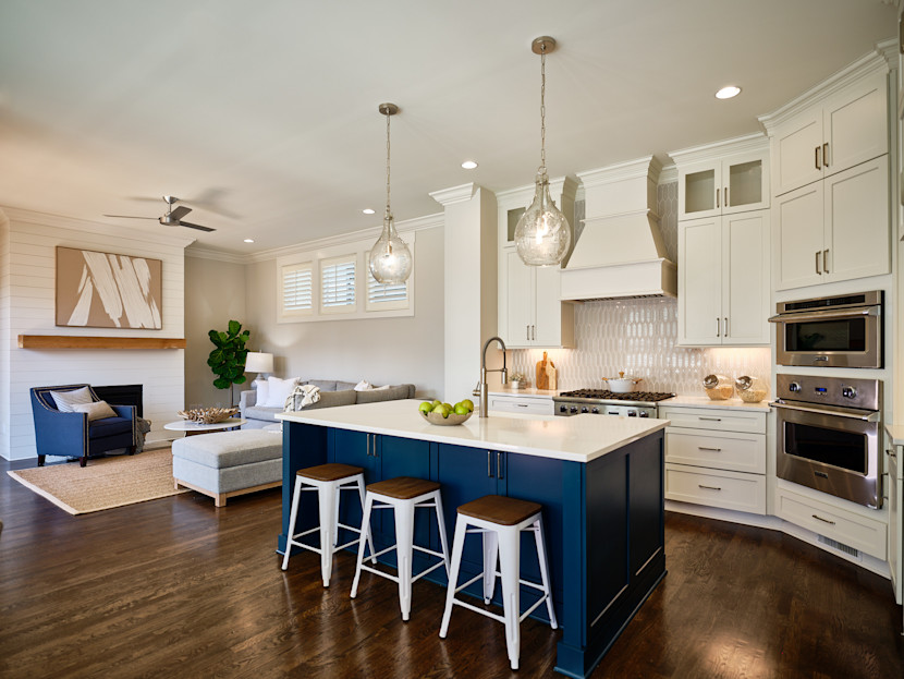 Modern kitchen with a kitchen island with blue cabinetry, white upper cabinetry, curved pendant lights, custom range hood, with living room nearby