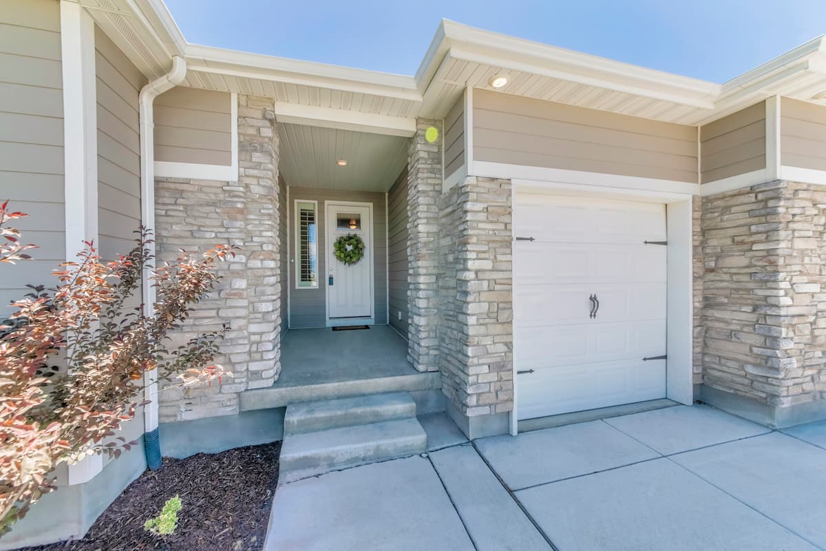 Exterior of home with white garage door, white front door with wreath and stone veneer