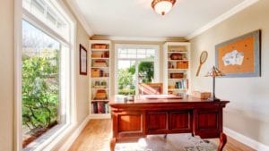 Office with a large window letting in natural light, an oak desk, and floor-to-ceiling shelves behind it.