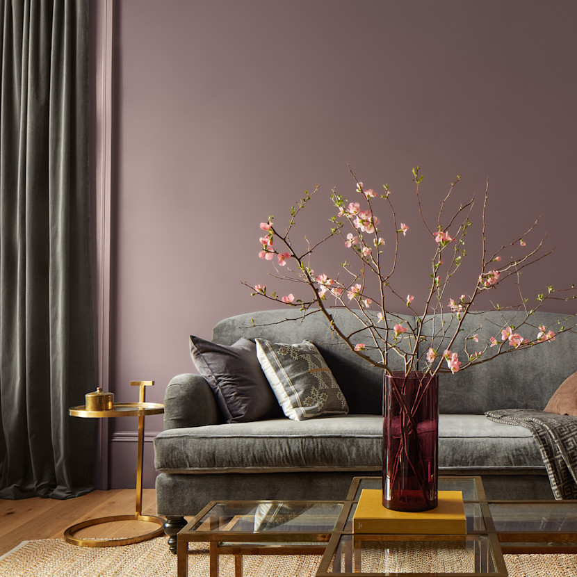 Living Room walls painted in Benjamin Moore's Cinnamon Slate, with vase with pink flowers on a coffee table in front of a grey sofa in the foreground