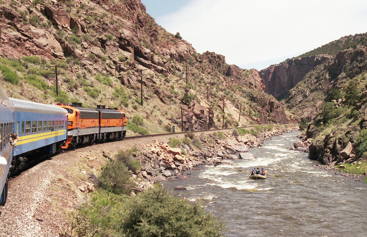 Train cutting through the Royal Gorge near raft riders in river