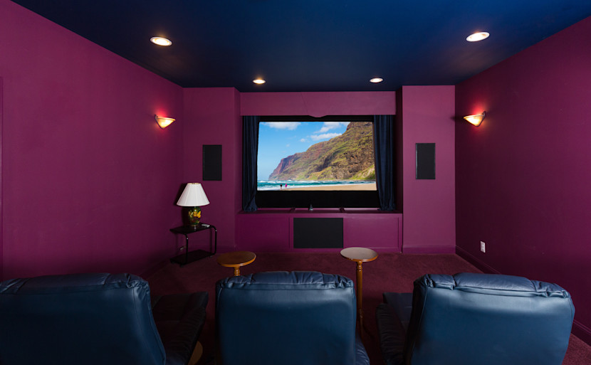 Media room with burgundy walls, potlights and movie on a large screen