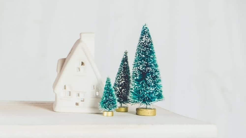 White ceramic house next to mini green pine trees.