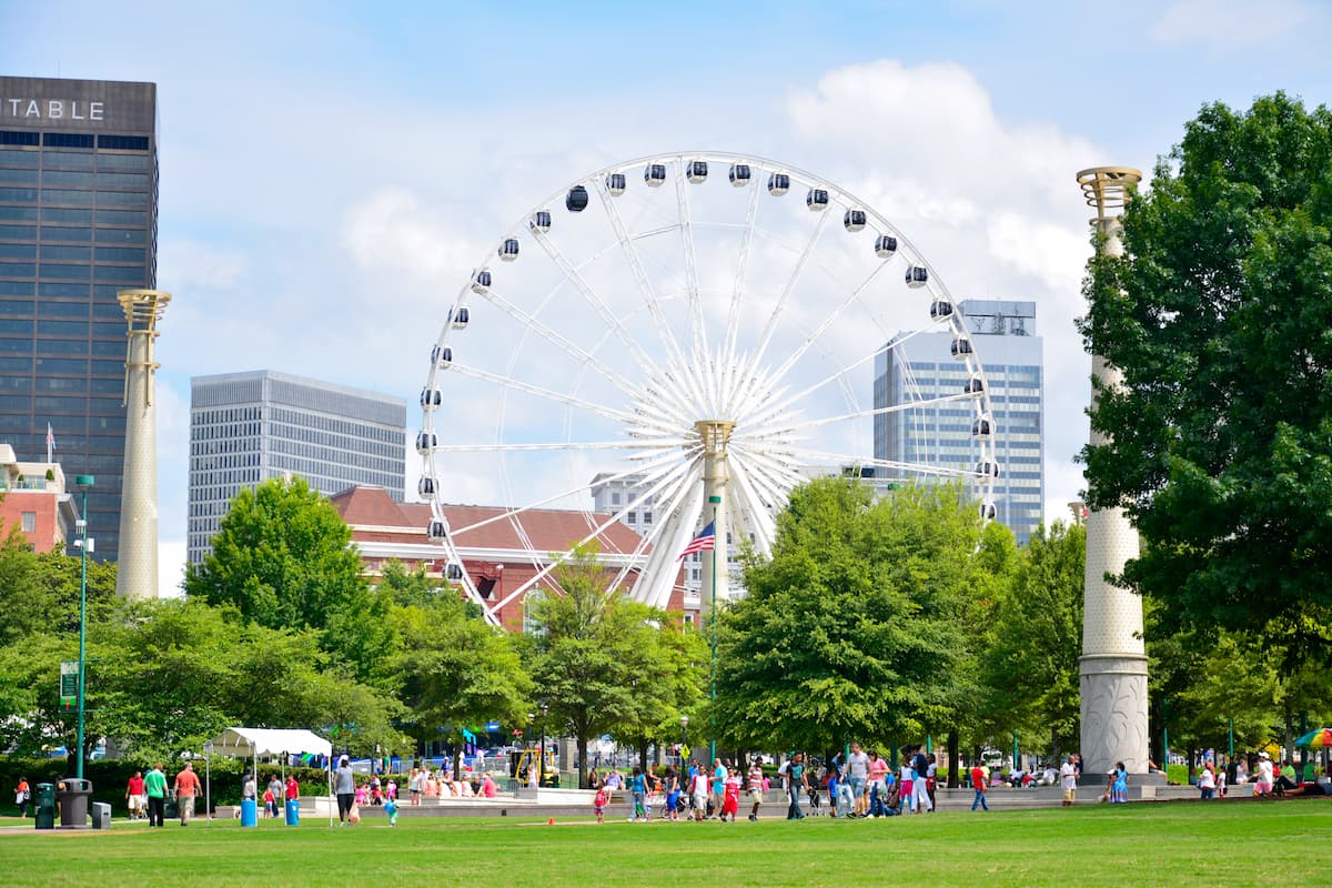 bustling park with ferris wheel, grassy area in foreground, skyscrapers in background