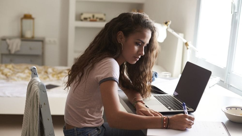 Teenager sitting at a desk in a bedroom.