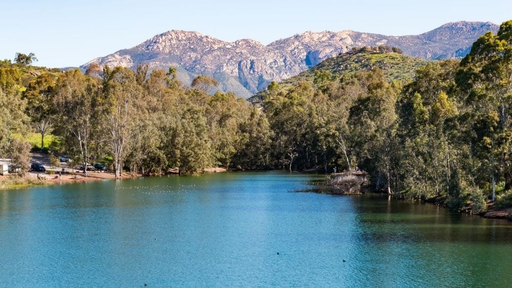 A clear blue lake with trees surrounding it and a mountain in the background.