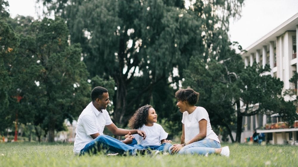 Family of three sitting in grass.