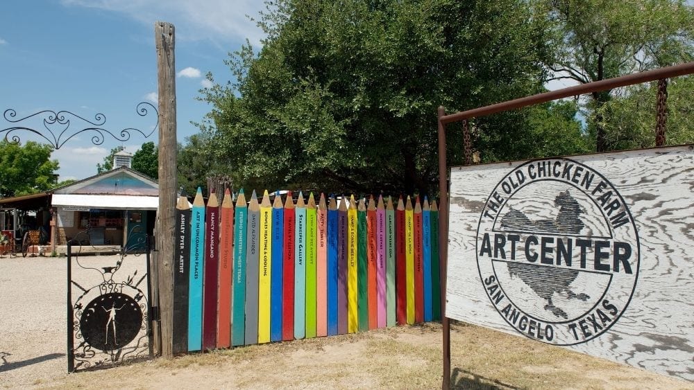 A colorful fence next to a sign reading “The Old Chicken Farm Art Center.”