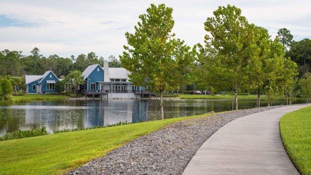 A sidewalk along a lake with a blue house on the edge.