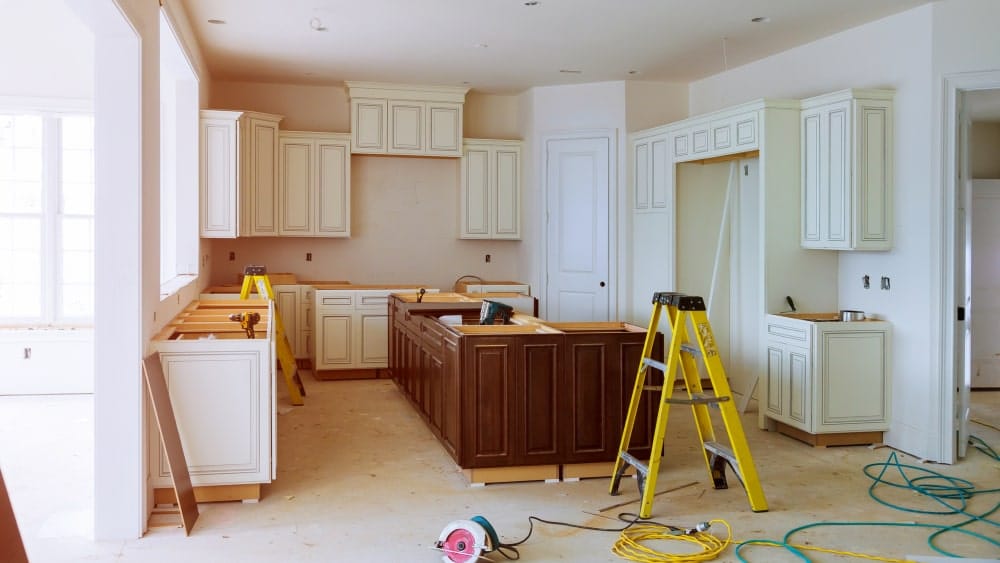 kitchen renovation showing white cabinets on walls and brown island cabinets with tools and yellow stepladder