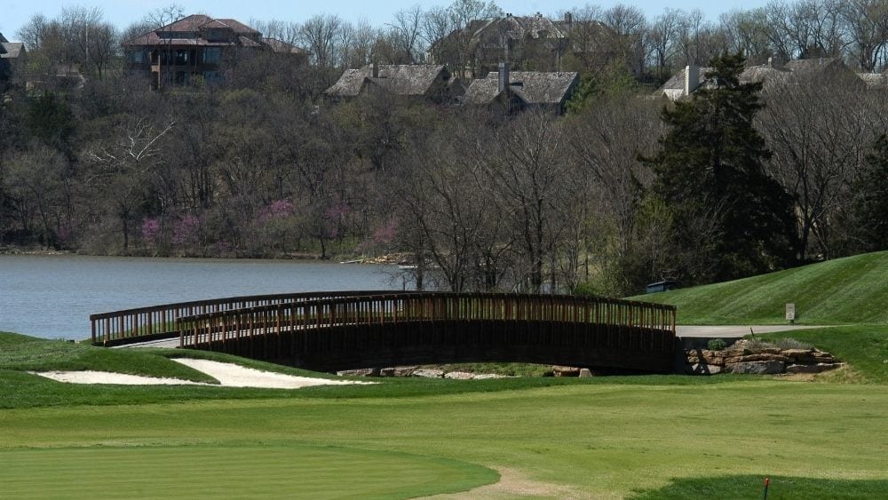 A long bridge next to a lake, surrounded by a golf course.