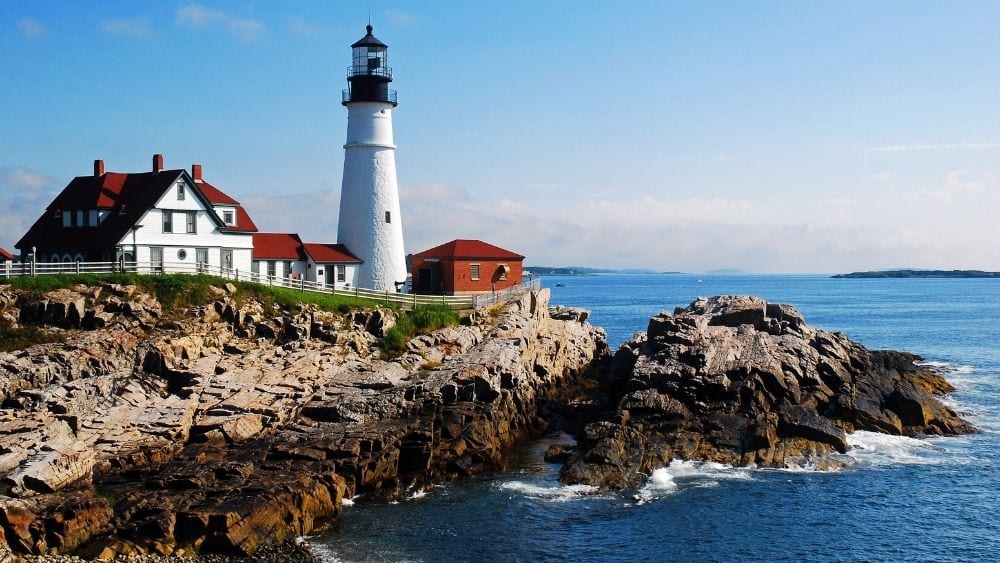 A lighthouse on an outcrop of land that drops into the sea.