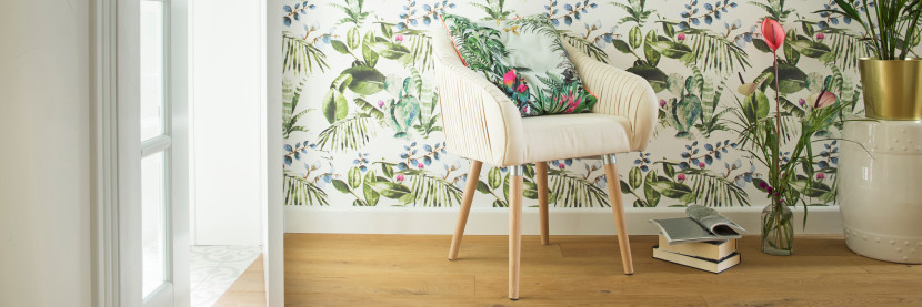 White armchair with botanical motif wallpaper, plants and reading material, near a large window
