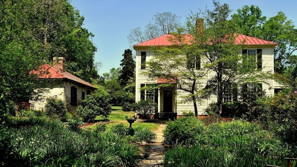 A large house with a red, barrel tile roof. A smaller structure sits next to it, and hedges line the property.