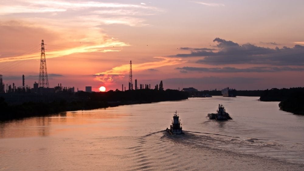 Two cargo ships moving away from the camera toward a sunset.