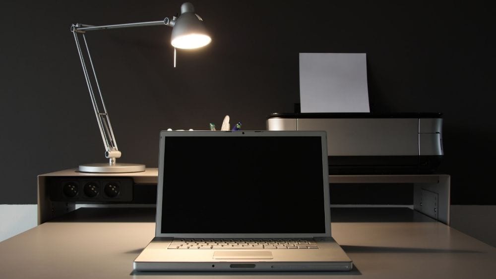 Open laptop with a task lamp behind it on a table.