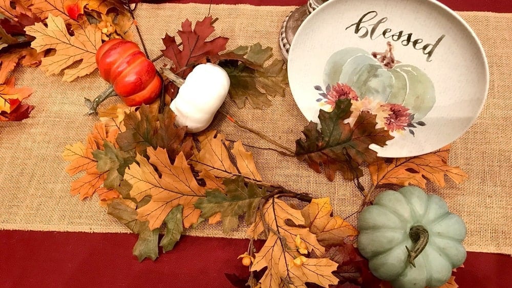 Table decorated with fall foliage, blue, white and orange pumpkins, and a plate painted with the word “blessed” and a blue pumpkin illustration.