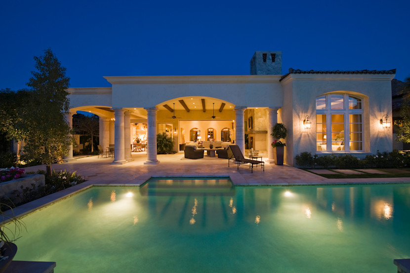 Backyard shot of a luxury pool with outdoor living area in the background, taken at night