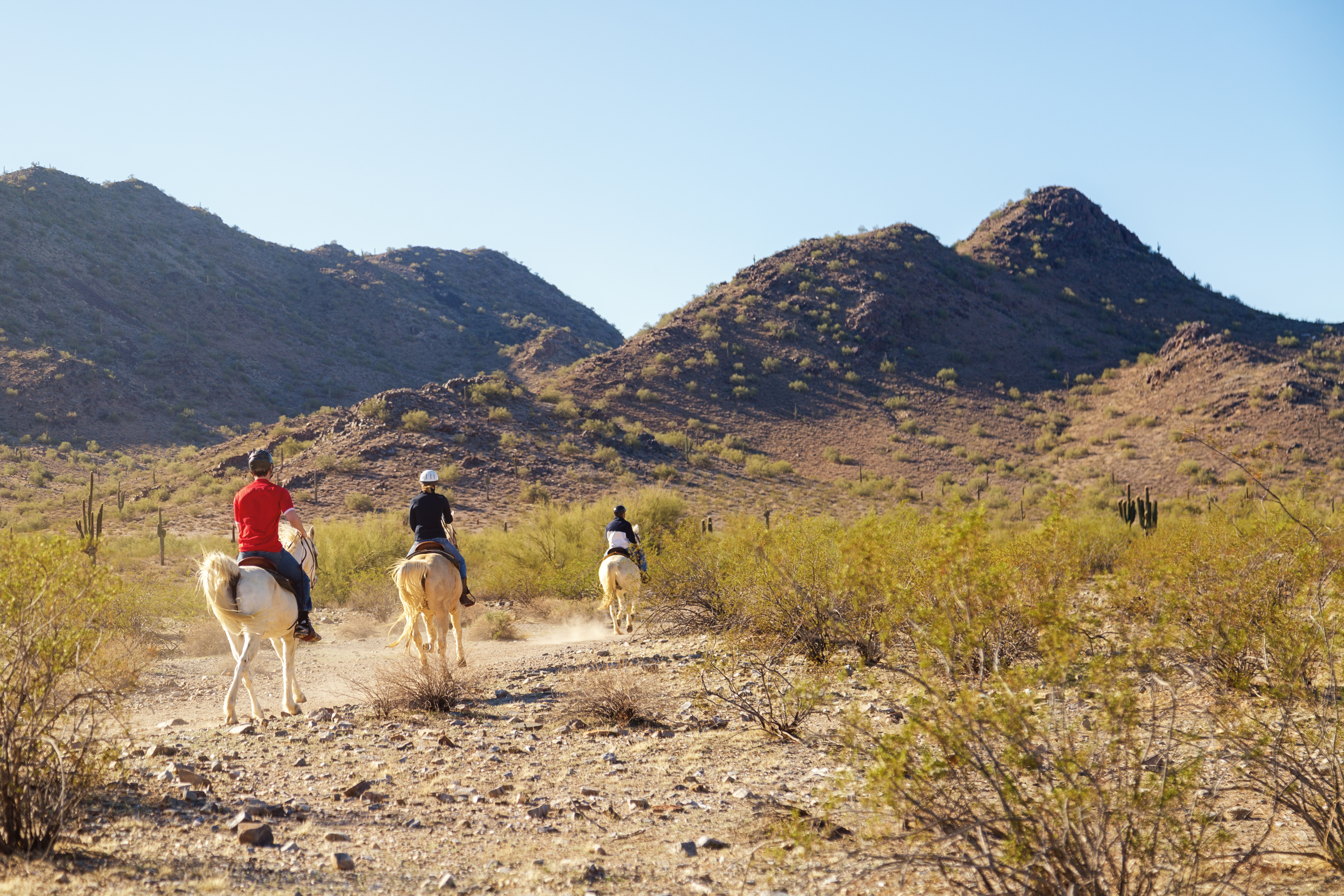 three people riding horseback through the desert terrain