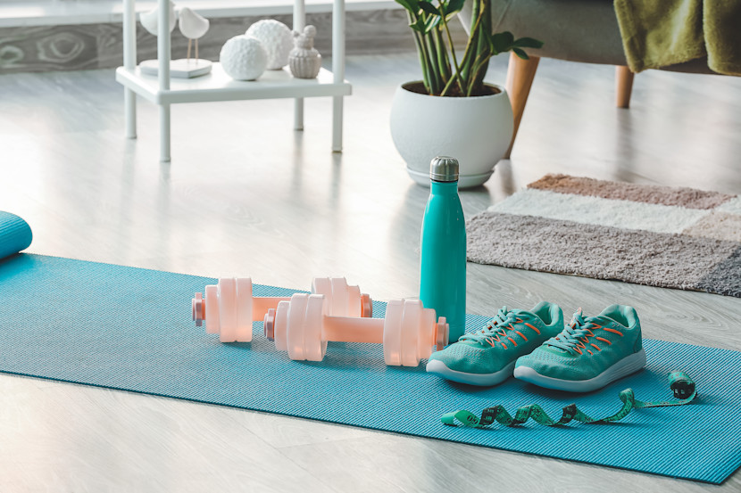 Yoga mat with water bottle, running shoes and hand weights in a home gym