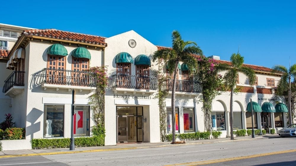 A strip of building fronts in Spanish style architecture with white stucco fronts and green awnings over the windows.