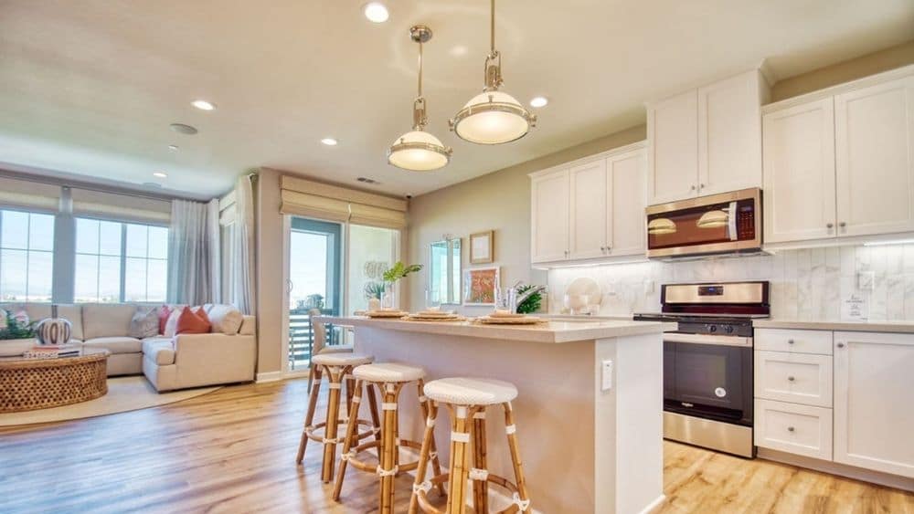 A kitchen with beach vibes: Hardwood floors, wooden bar stools, and light colored cabinets and counter tops.
