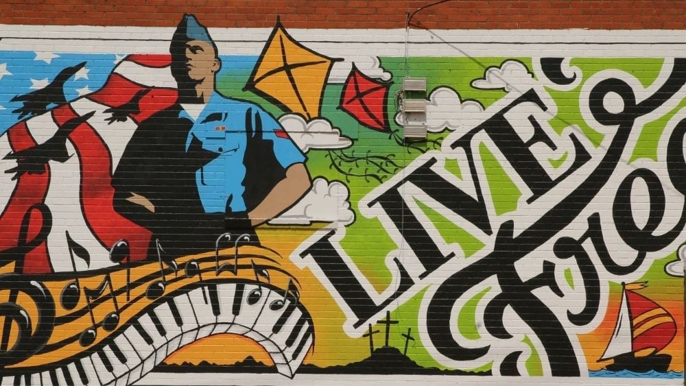 Graffiti of a soldier standing at parade rest next to the words “live free.”