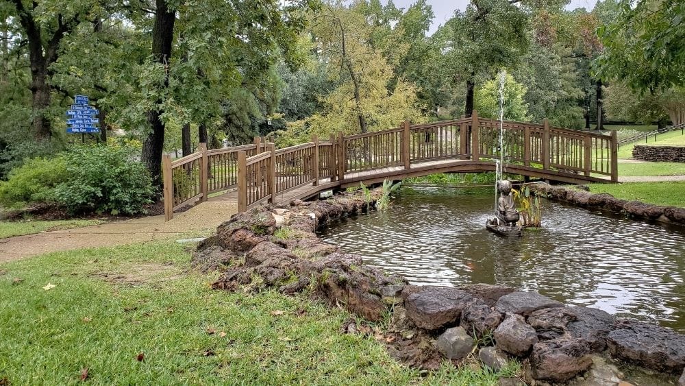 A rose garden with a stone pond and bridge.
