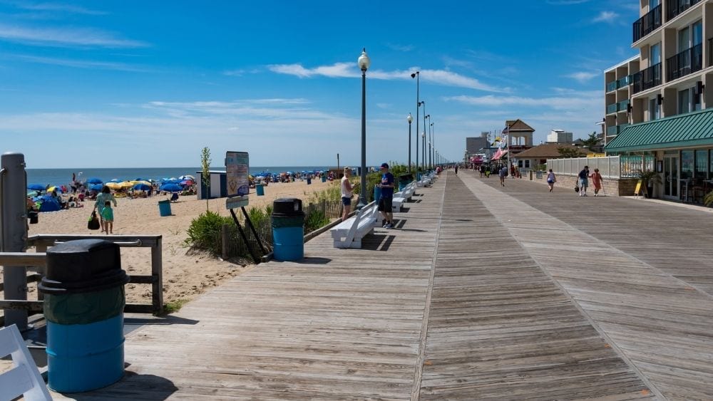 Boardwalk on a clear day with people looking at shops and sitting on the beach.