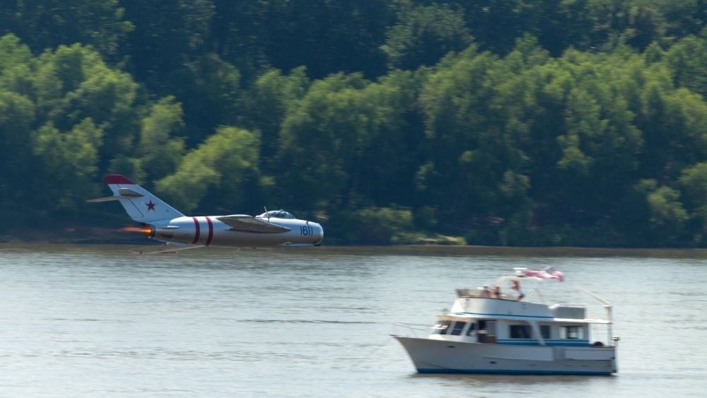 A plan flies over a personal boat out on the river during an air show.