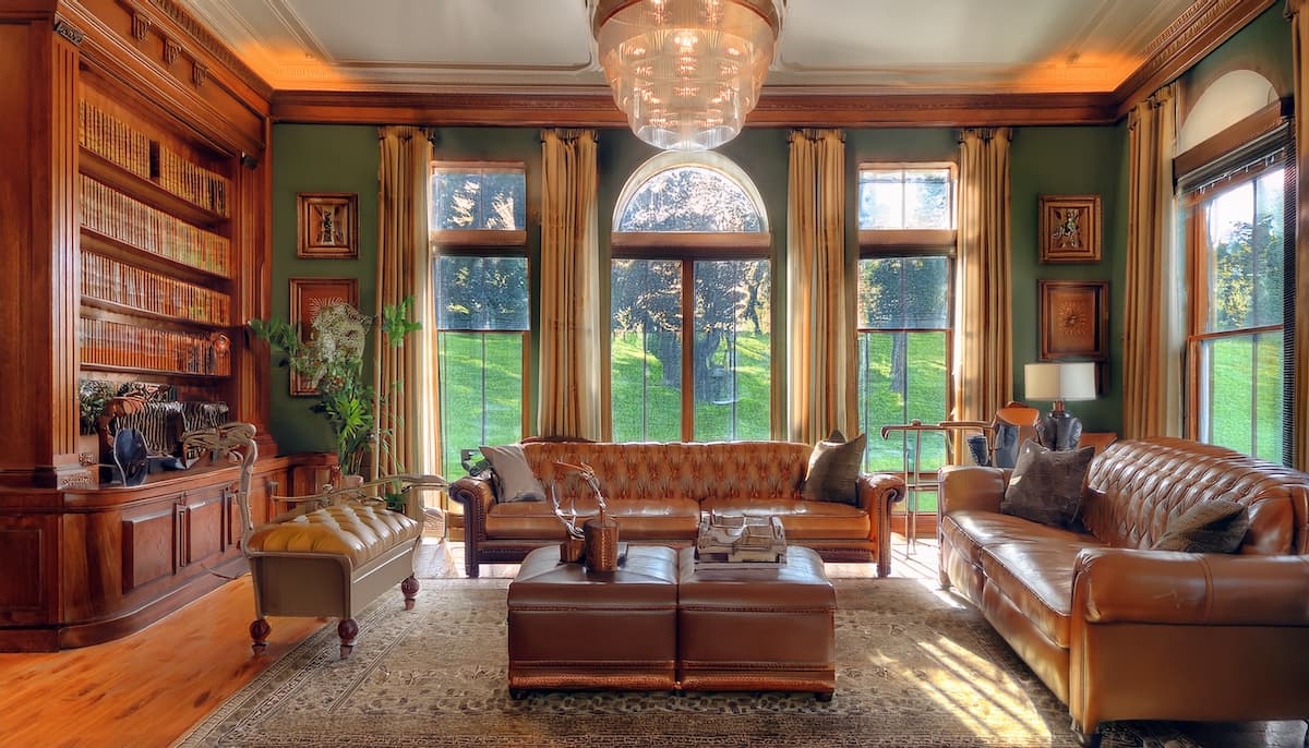 living room styled in country club core with bookshelves, brown leather sofa, hunter green walls and a steamer trunk coffee table