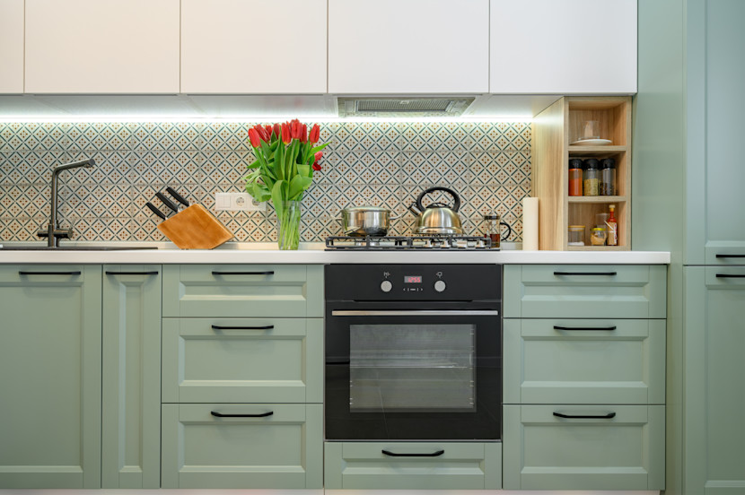 Green lower cabinets with white uppers, black oven, gas stove and red tulips in a vase