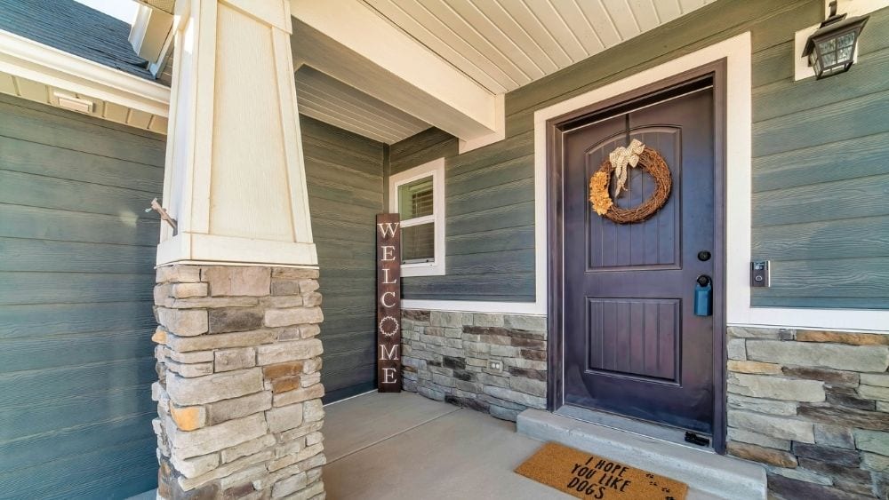 Front porch of a home with wood siding painted blue and stone facades on the lower half of the wall.