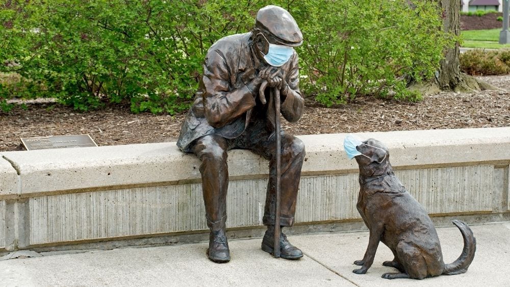 A statue of a man with his dog, both wearing PPE face masks.