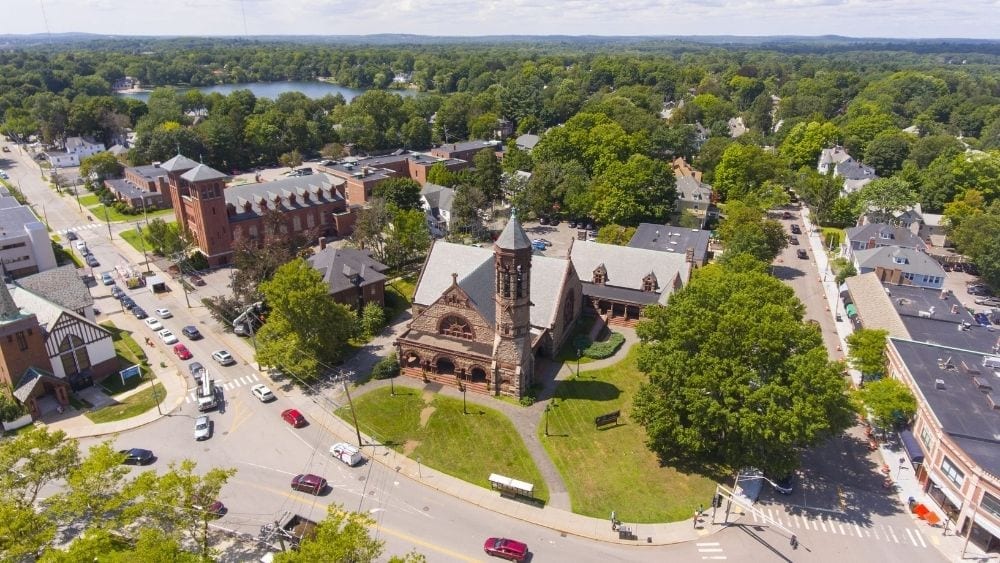 Aerial view of an old church on the corner of a wide street with lots of trees around it.