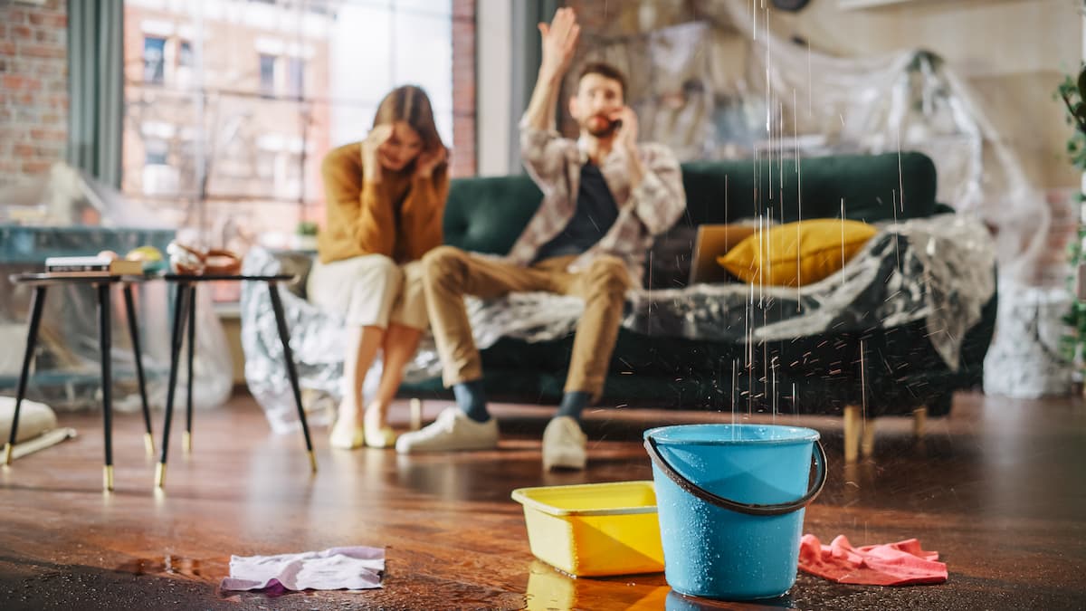 Family dealing with the stress of a leaking roof while sitting in their living room. Floor covered with towels and buckets. 