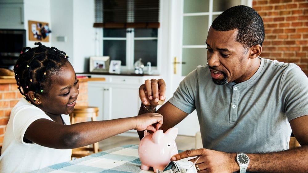 Dad and daughter putting coins in a piggy bank