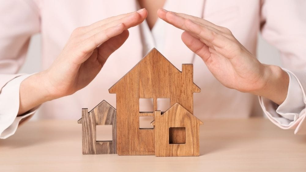 Hands arched over a small replica of a house, symbolizing home warranty coverage.